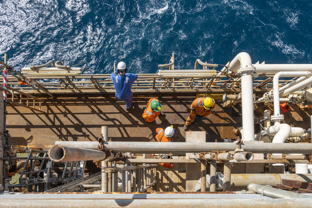 Workers in safety helmets standing on an offshore oil platform above the ocean.
