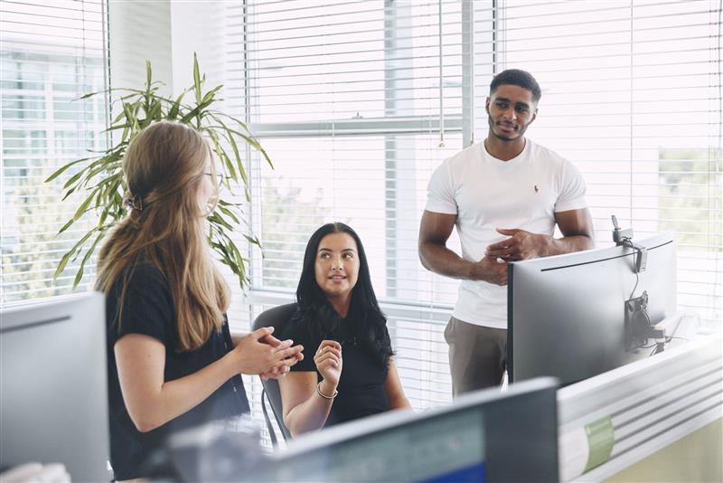 Three coworkers discussing in a bright office near computers
