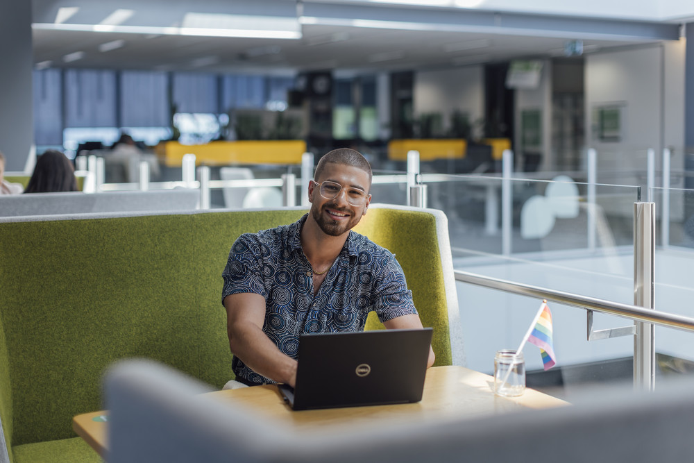 Smiling man working on a laptop at a booth in a modern office space.